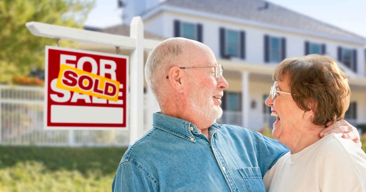 senior couple in front of sold real estate sign