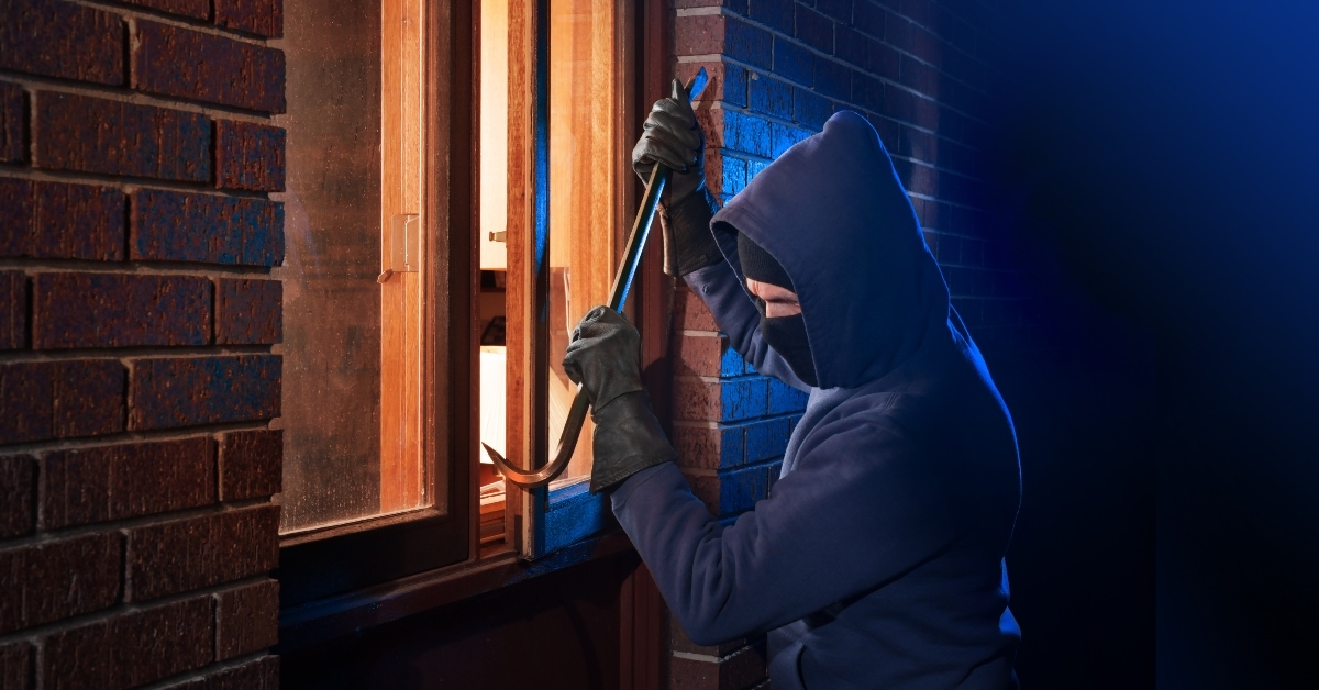 burglar using crowbar to break into a house at night