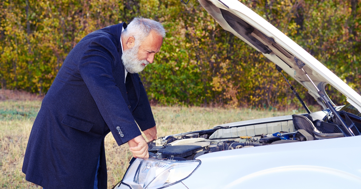 senior man looking under the hood of breakdown car