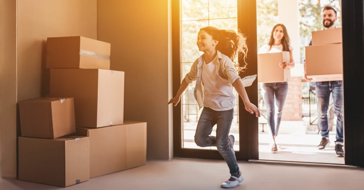girl running into her new home as her parents hold moving boxes in their hands