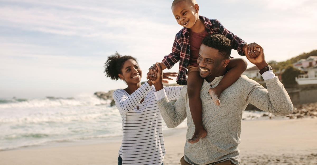 parents carrying son on shoulders on beach vacation