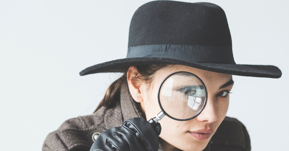 young woman dressed as a detective, looks through a magnifying glass