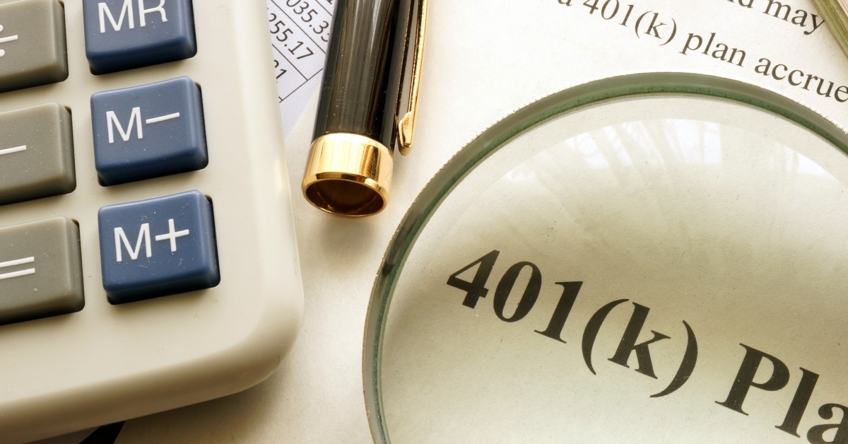 magnifying glass on document with 401k plan besides calculator on table