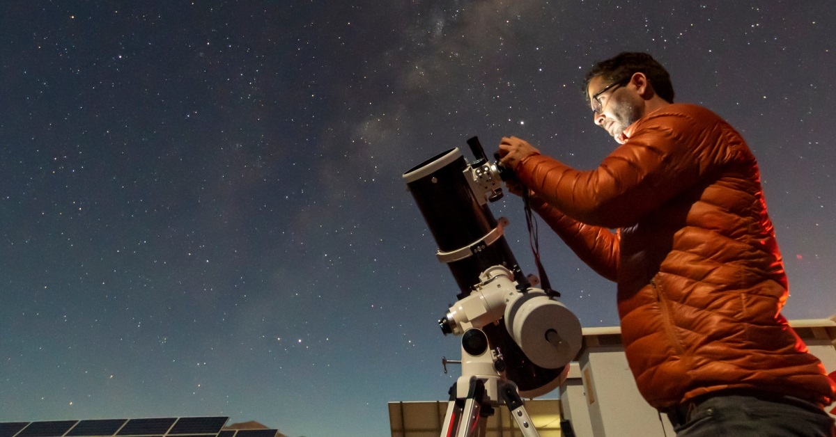 man with with a huge telescope, staring at the sky during the night.