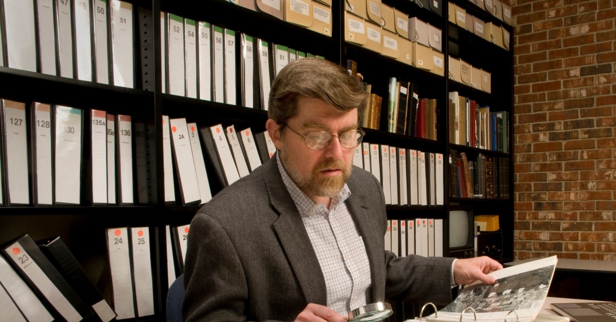 investigator in the record room going through records using a magnifying glass