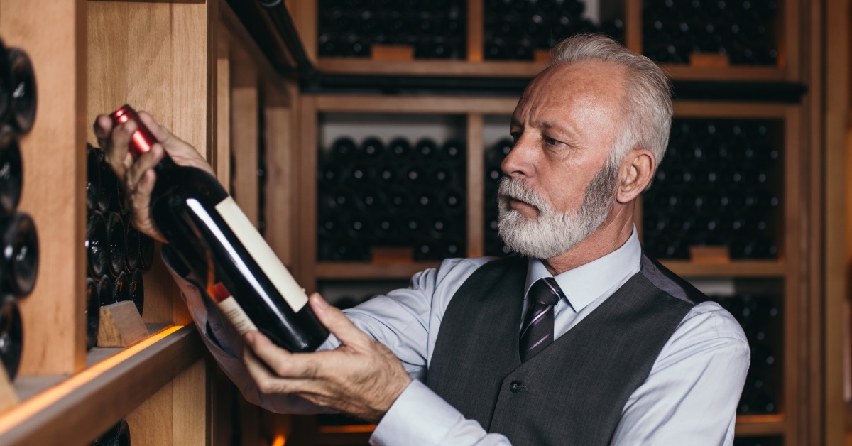 senior man in suit checking out a wine bottle from the shelves