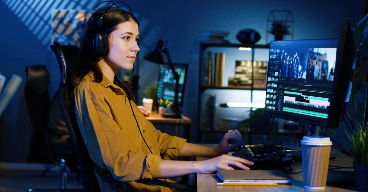 young woman wearing a headset is working on a desktop computer in the dark
