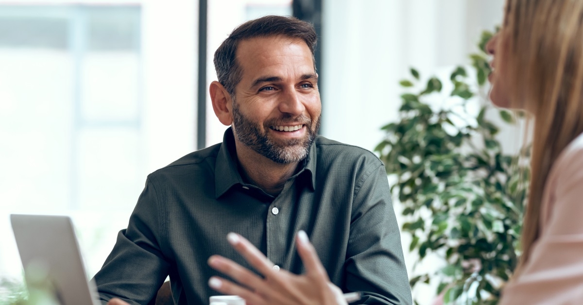 two happy colleagues sitting talking to each other in front of laptop
