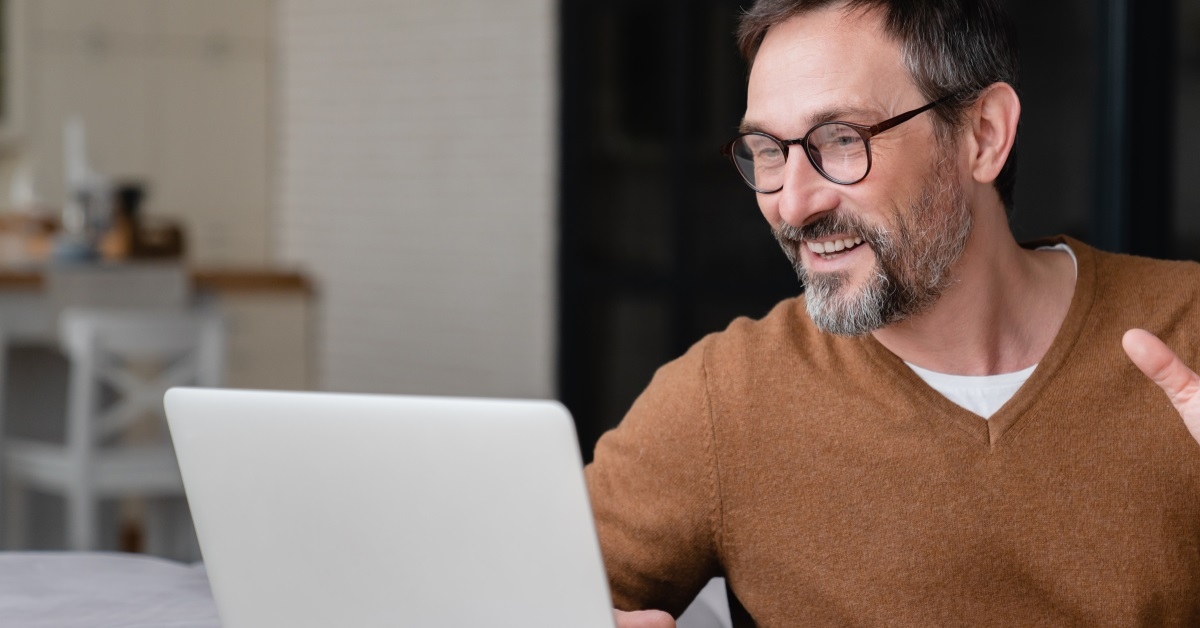 happy mature man waving hand in front of laptop