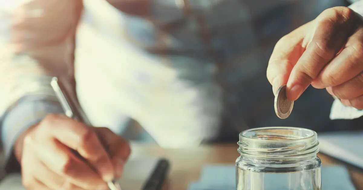 man putting pennies into jar while writing something on notebook