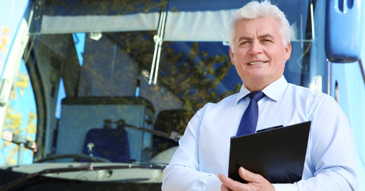 senior man with clipboard standing in front of bus