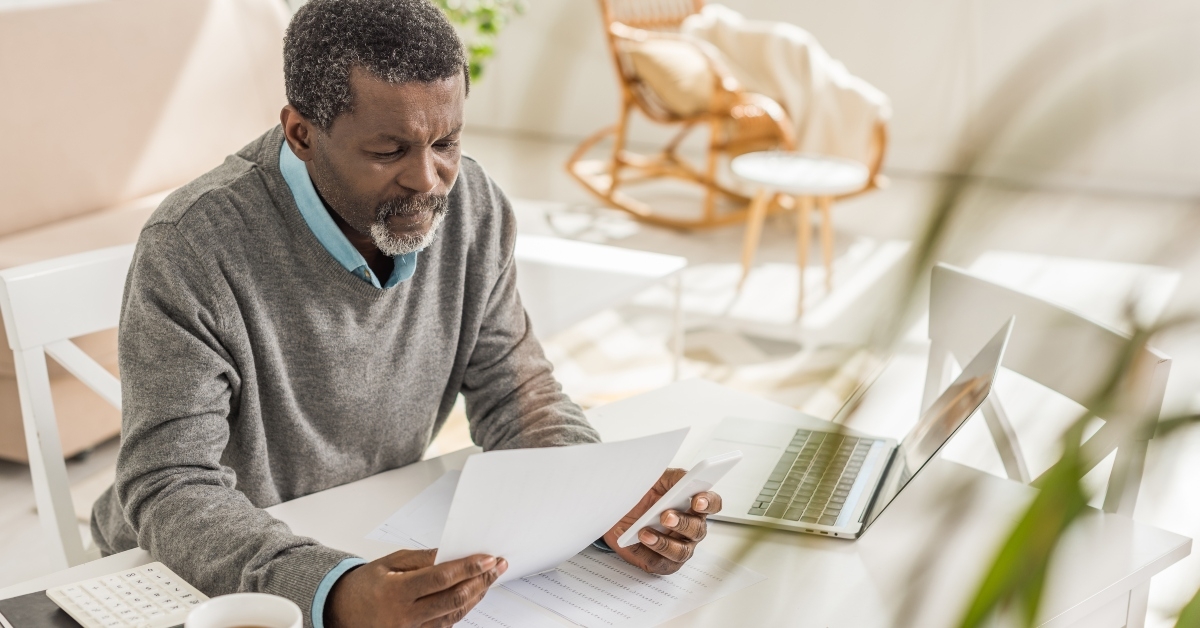 man looking at utility bill while sitting near laptop