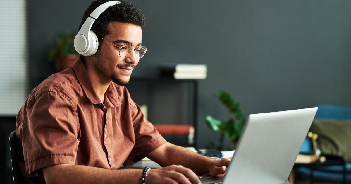 smiling man in headphones typing on laptop