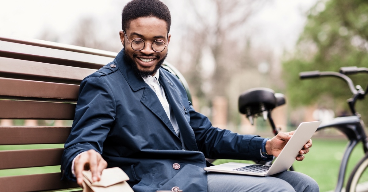 african american man using laptop outdoors while enjoying snacks