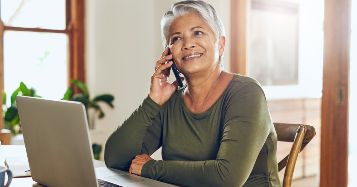 senior woman sitting in front of laptop smiling while talking on phone