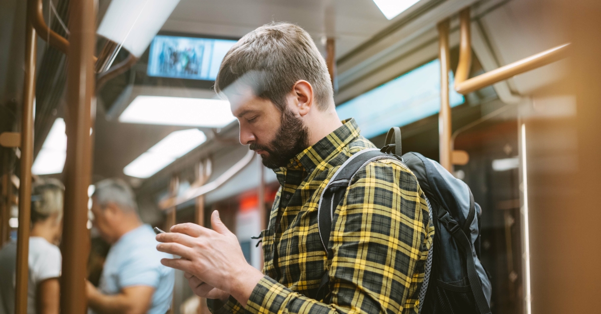 man standing in subway car holding mobile telephone