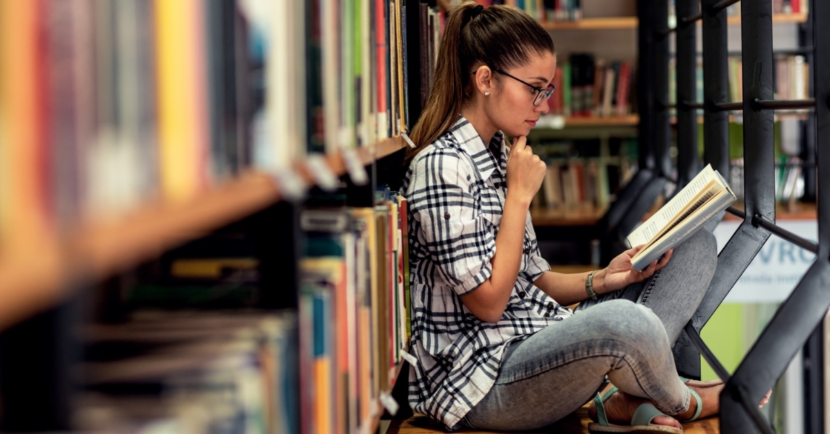 young woman sitting besides book shelf in library 