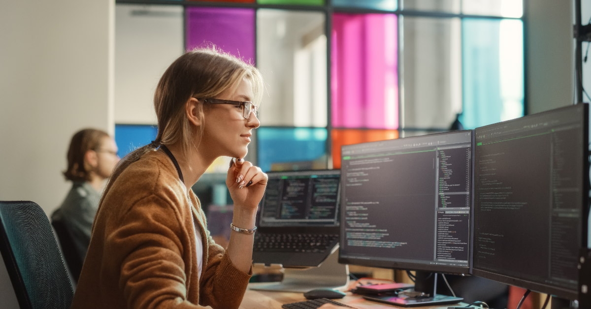 woman at workplace working on codes using two monitors