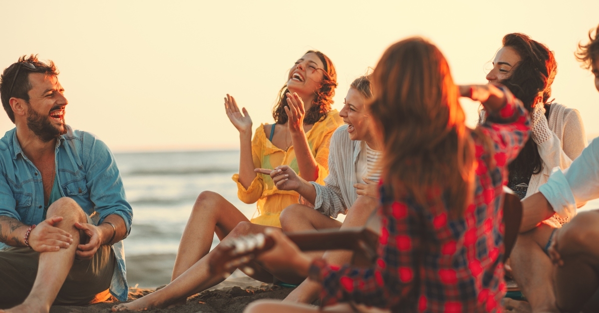 friends sitting on the beach singing and playing guitar