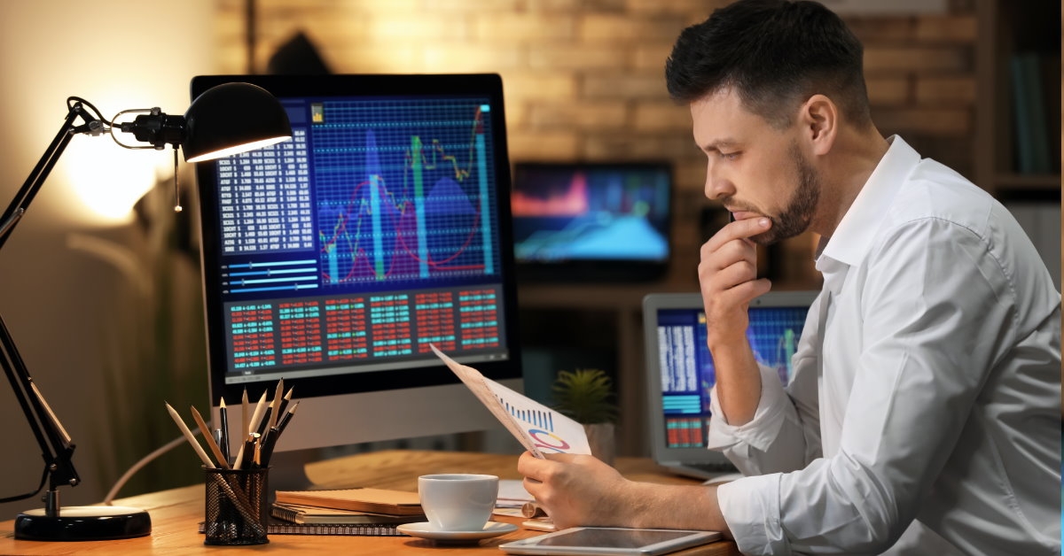 young stock exchange trader analyzing papers while sitting in front of laptop