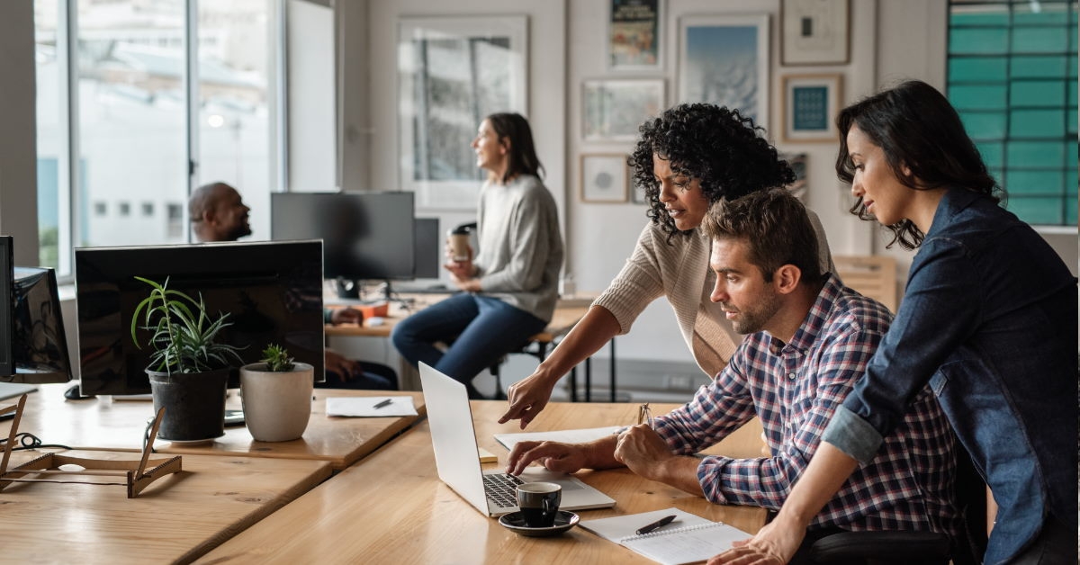three young employees working on laptop together in office