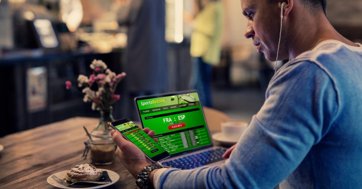man using smartphone and laptop to bet on online sports