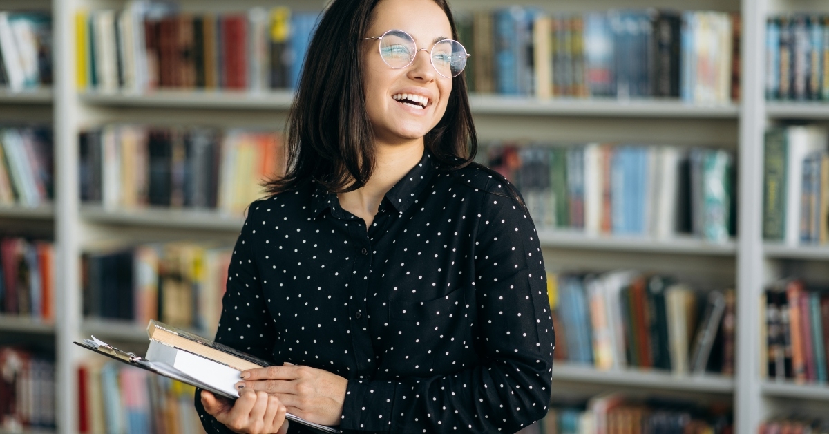 student in formal shirt and eyeglasses holding books