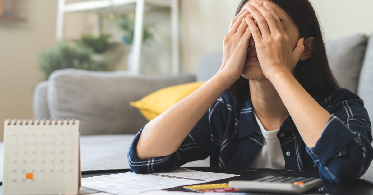 woman covers her face in distress as she contemplates her expenses