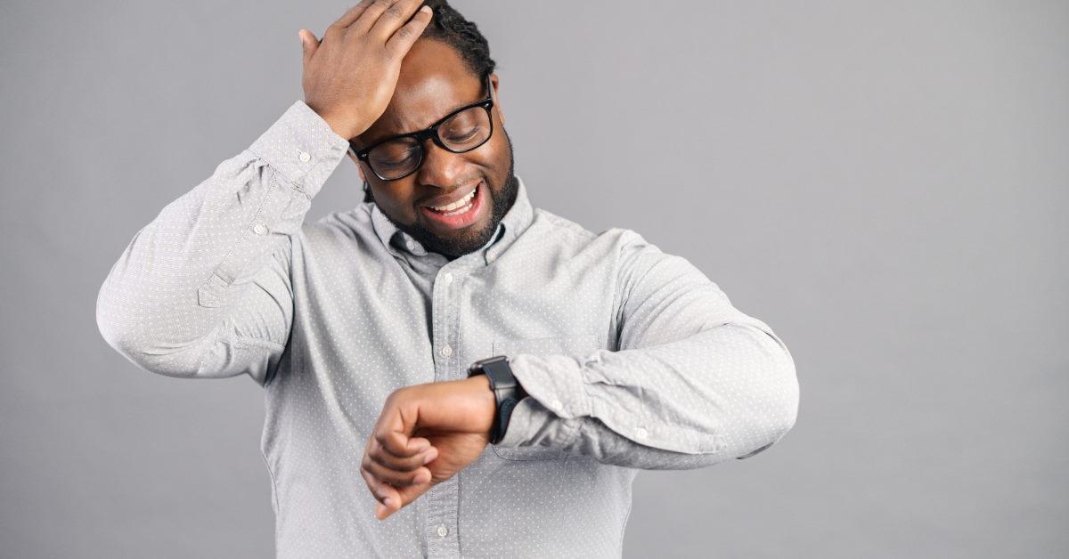 african american man wearing white formal shirt looking at watch while holding head 