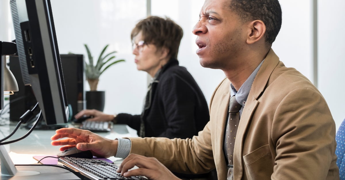 african american man sitting in front of monitor squinting eyes at work 