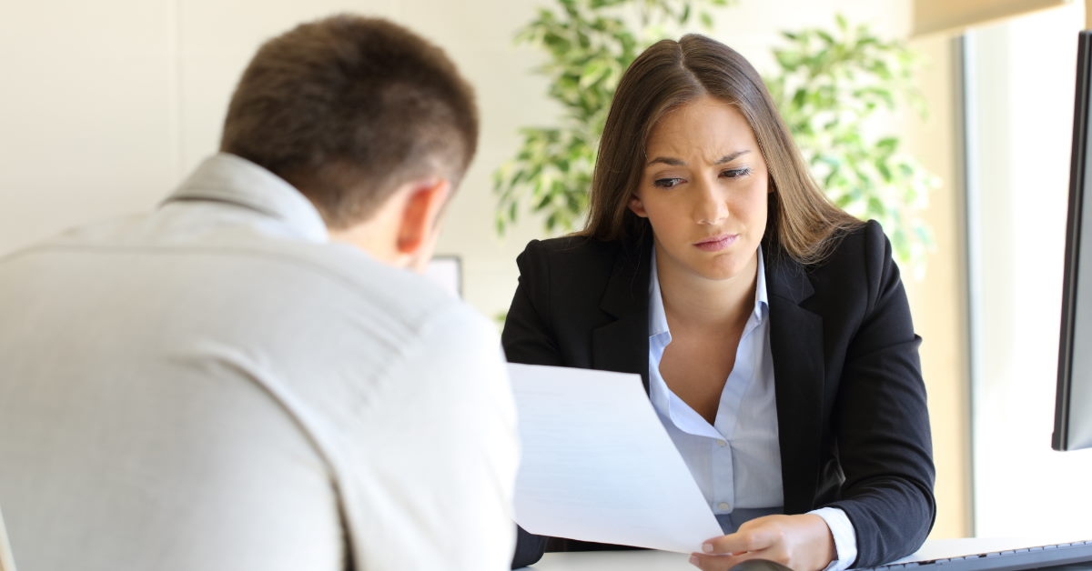 businesswoman looking at resume of a man sitting in front of her 
