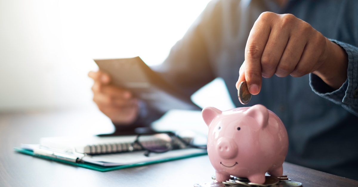 hand putting coins in pink piggy bank 