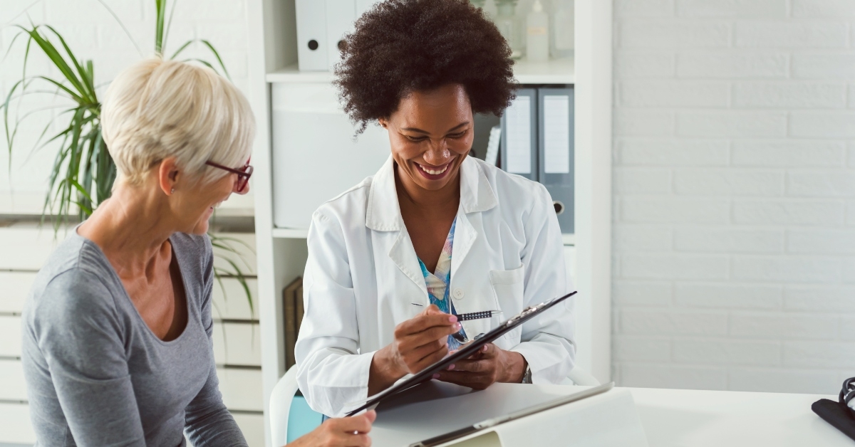 female doctor sits at her desk and chats to an elderly female patient