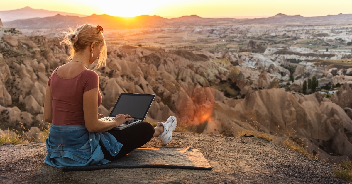 young girl working at laptop at sunset on top of mountain