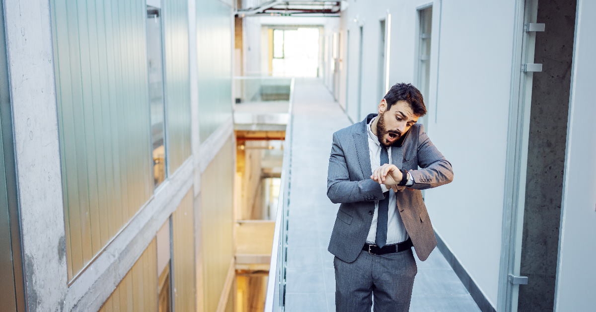 businessman walking in corridor checking wrist watch while talking on phone