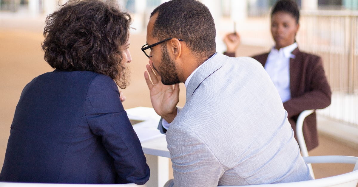 colleagues sitting at table gossiping about female boss sitting in front of them