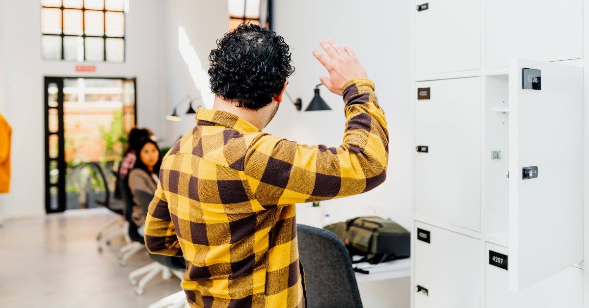 man standing in front of lockers waving hand at employees in the background