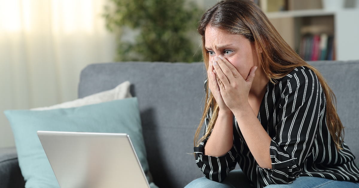 woman sitting in front of laptop covering her face in despair