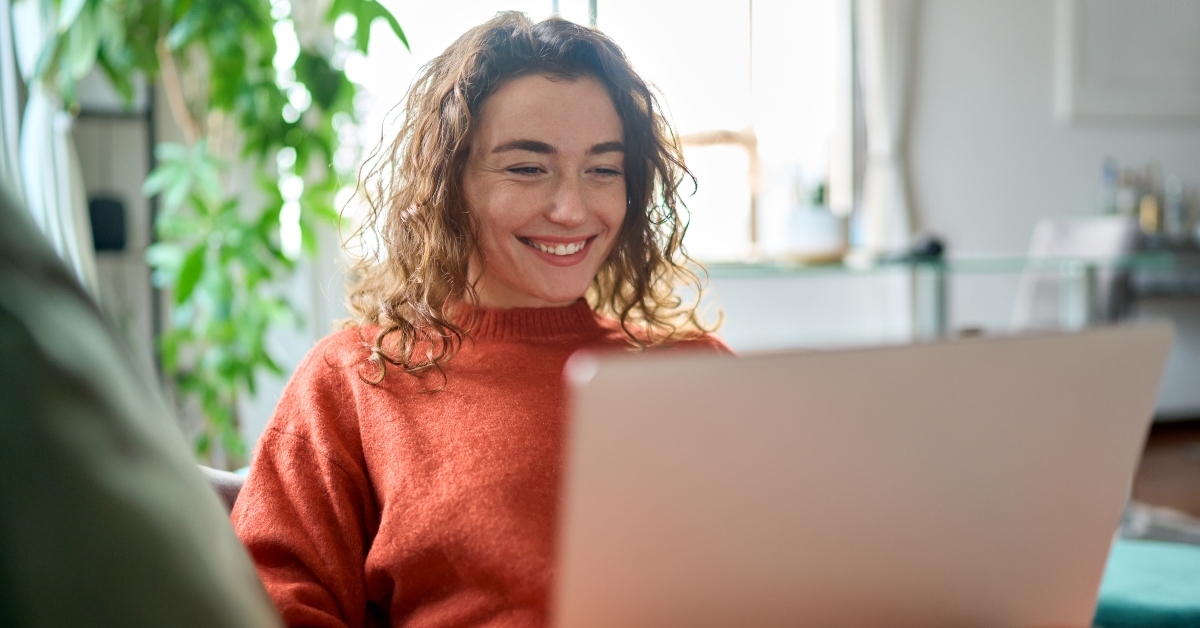 young woman sitting on sofa using laptop at home surfing