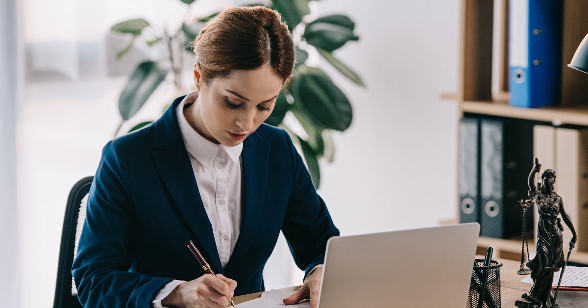 female lawyer sitting on table in front of laptop signing papers