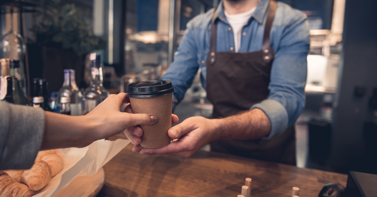 female hand taking cup of hot coffee from barista