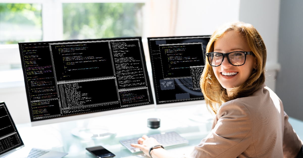 happy woman sitting on chair coding on two monitors