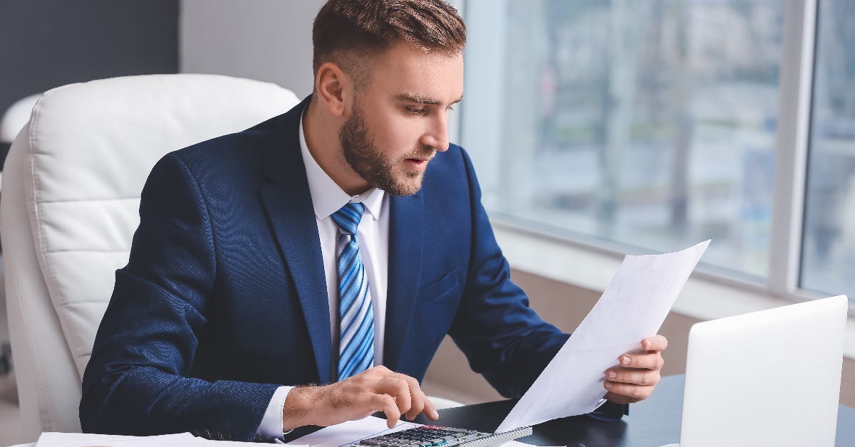 male accountant sitting across table checking document while using calculator