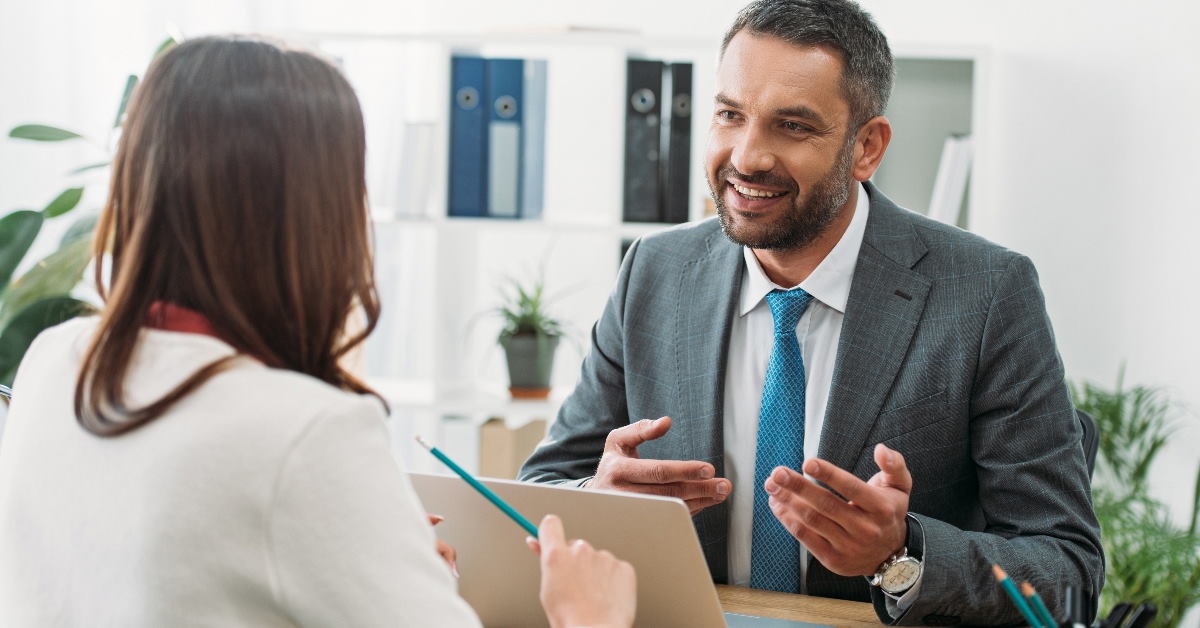 male advisor sitting at table in office talking to female in front of him
