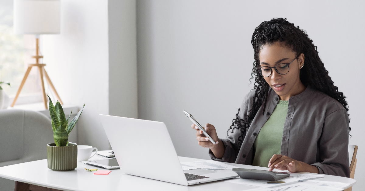 african american female accountant sitting at table in front of laptop using calculator