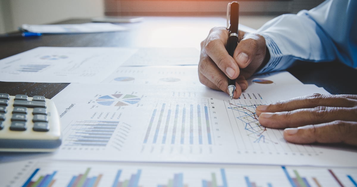 man using pen to check business graphs on papers at work