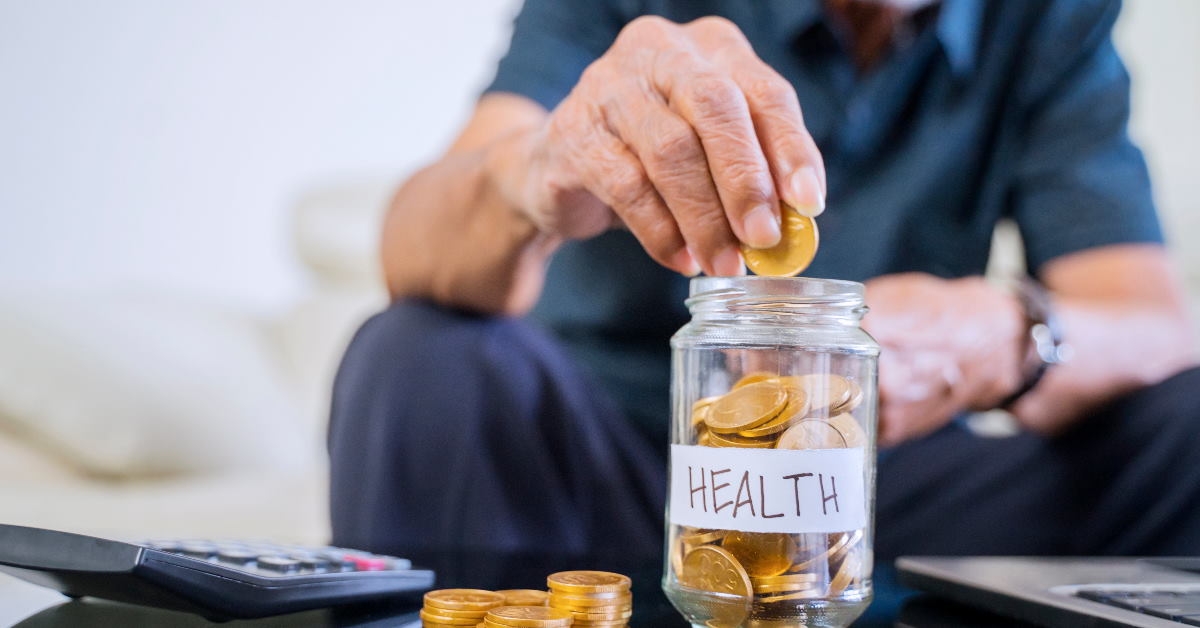 old man sitting on couch in front of table saving pennies in glass jar 