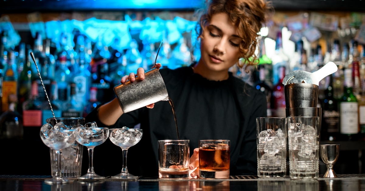 female bartender preparing cocktail and pouring it into glass