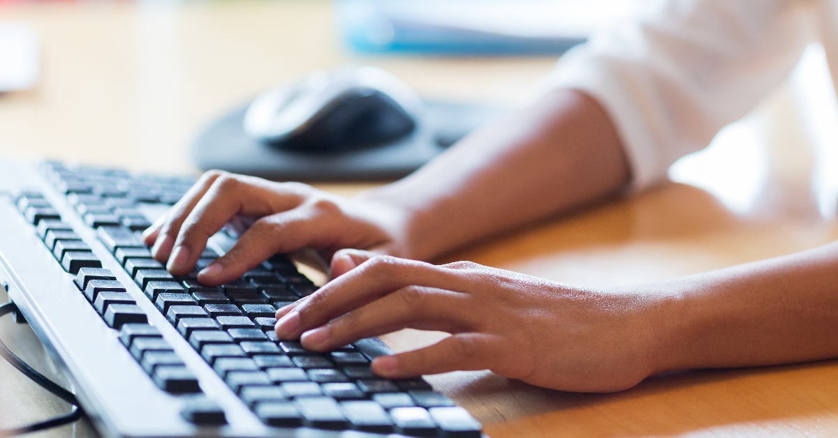 hands typing on keyboard at wooden table