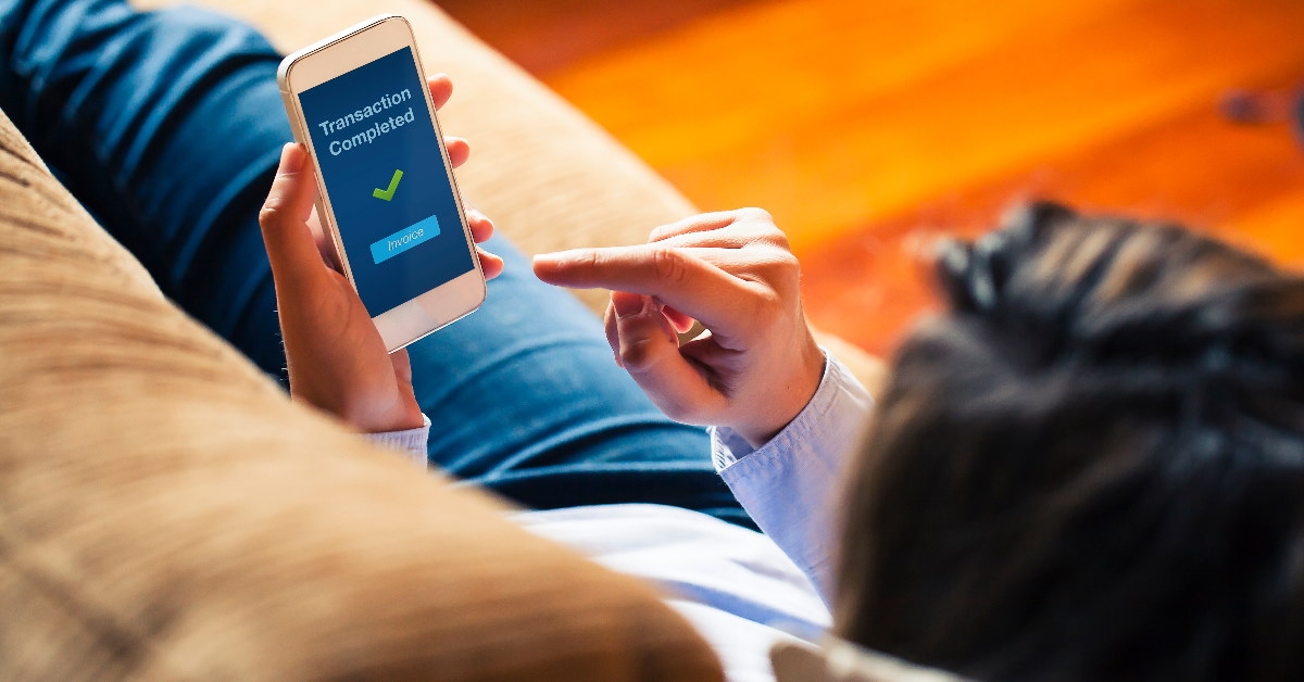 woman sitting in front of laptop at table reviewing documents in hand